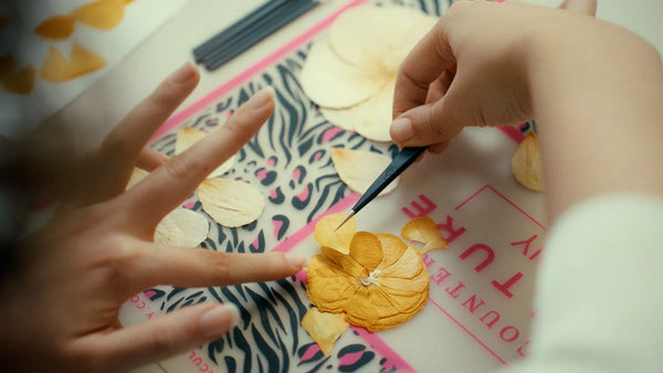 artisan arranging pressed flowers inside frame around an invitation before sealing