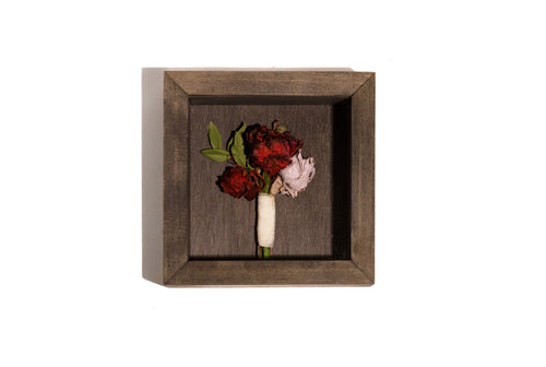 Dark wood shadow box with single boutonniere flowers center framed.