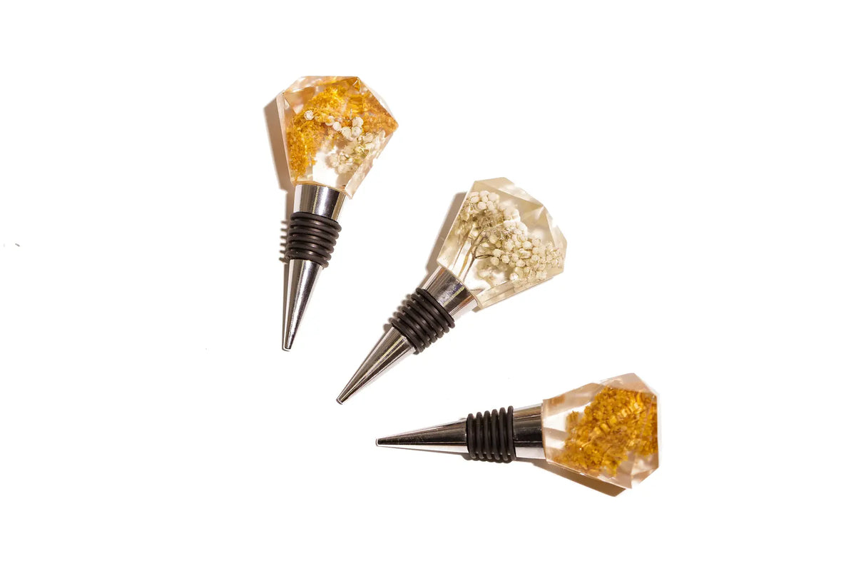 Three diamond-shaped wine bottle stoppers with preserved flower tops.