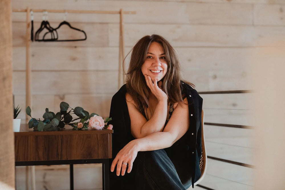 Woman sitting in a cozy room with wooden walls and a small table with plants.