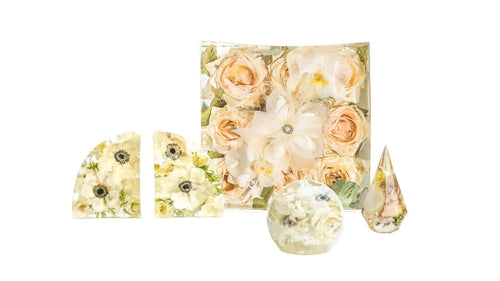 A large square bouquet block, two preserved flower bookends, a free standing sphere with white flowers, and a ring holder made of resin.