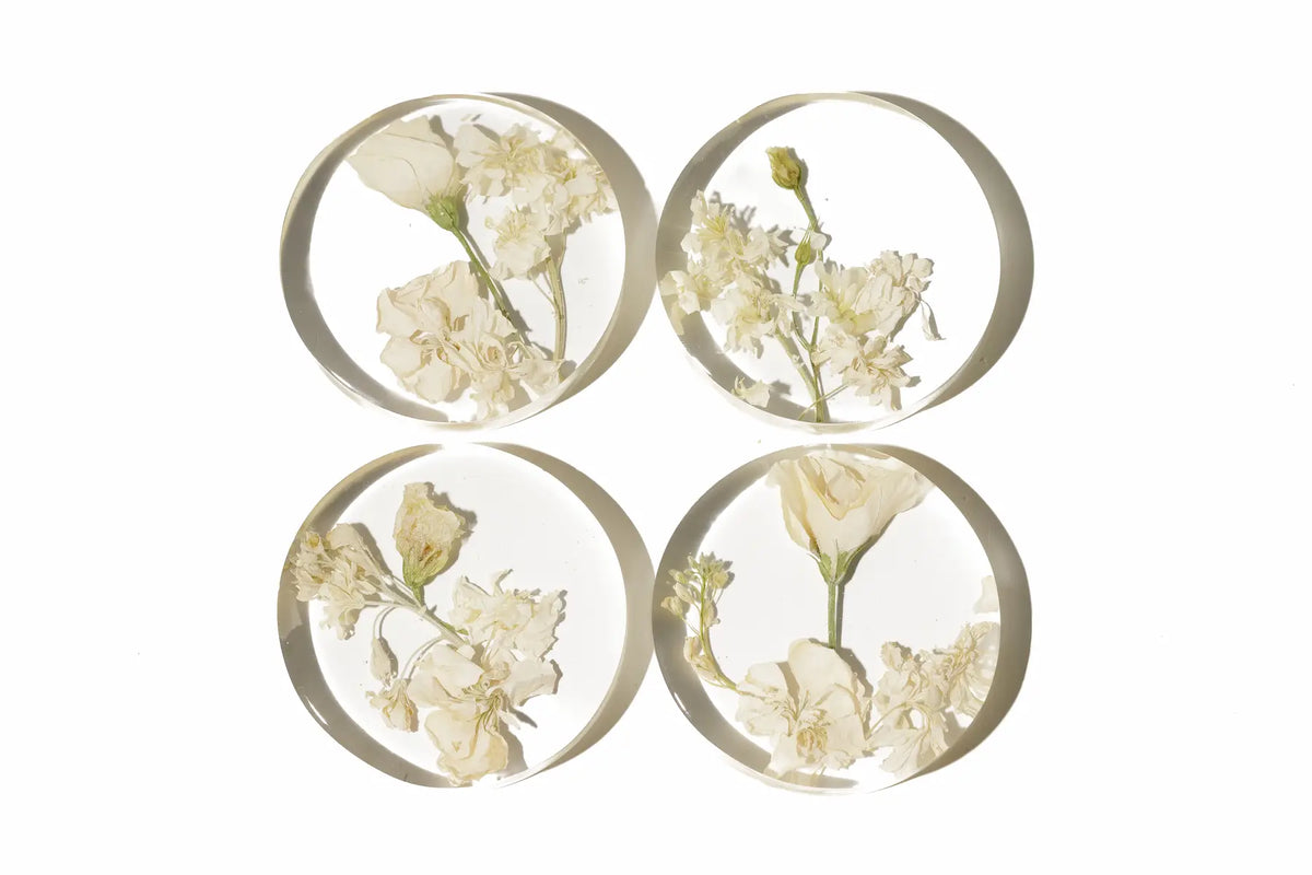 Four circular resin coasters with pressed and preserved flowers on a white background