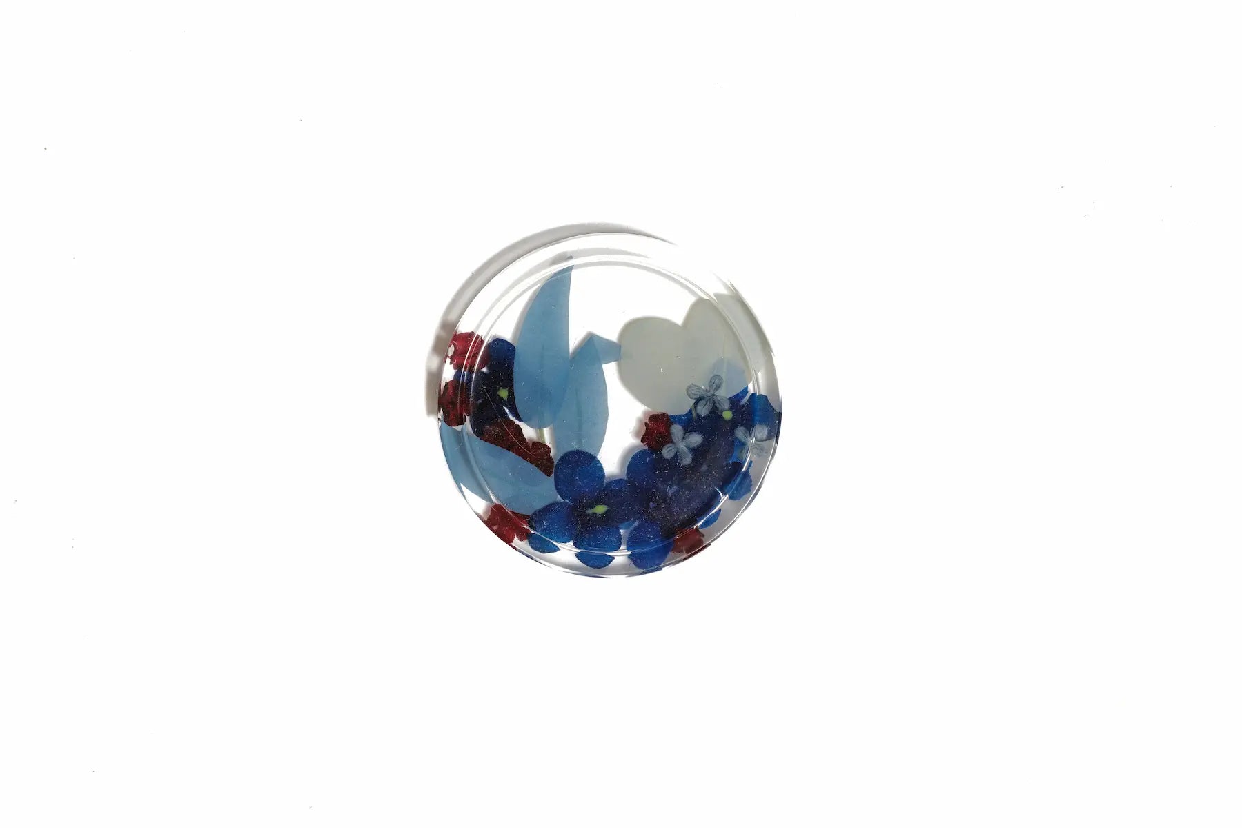 A 6 inch circle catch all dish made of resin to preserve the blue flowers inside of it