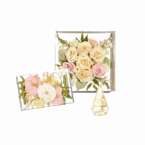 A large square bouquet block with a bridal bouquet of white roses, a resin serving tray with preserved pink flowers, and a ring holder with a white rose.