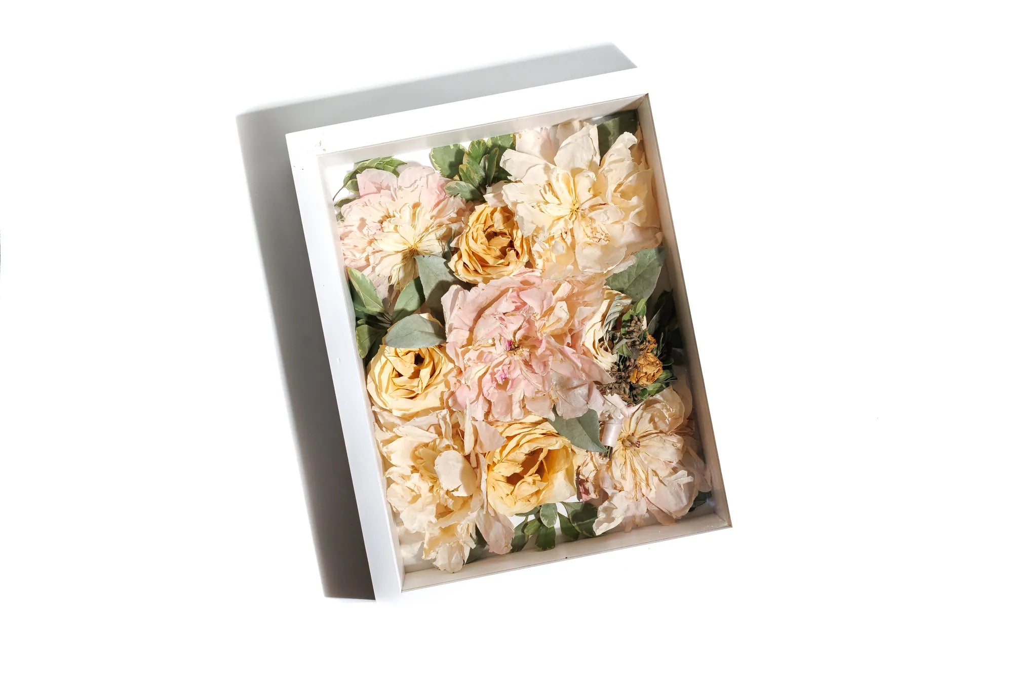 Shadow box of preserved flowers with pink and yellow hues in a white frame