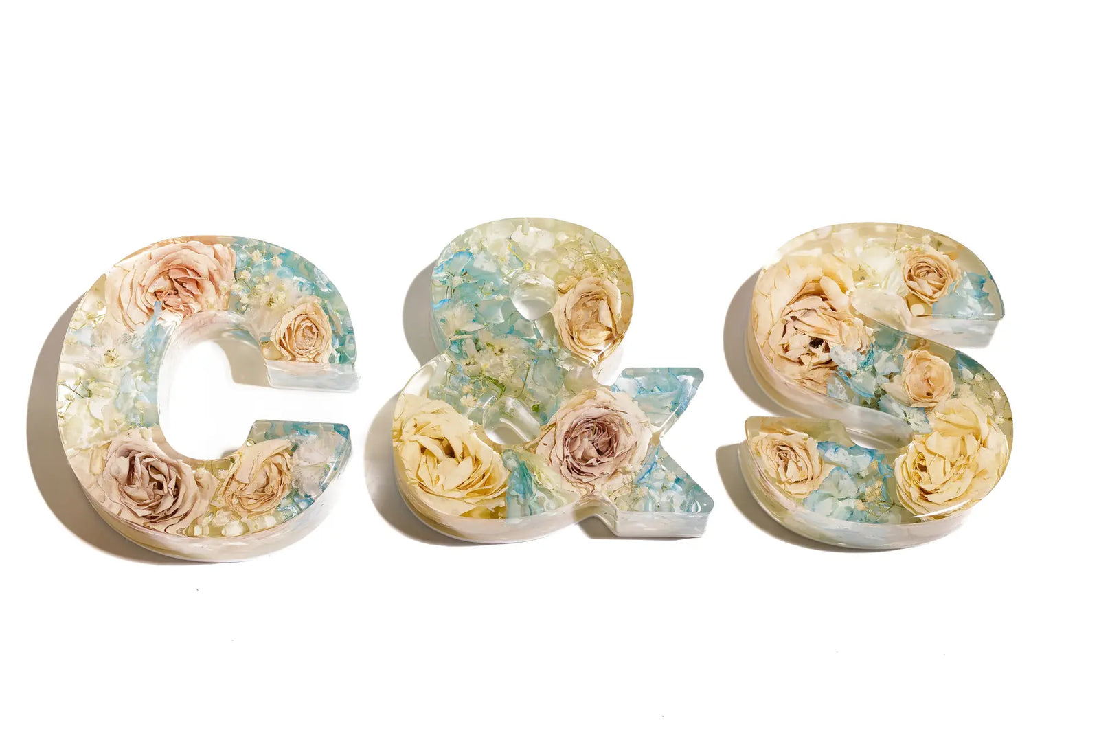 Decorative resin letters 'C', '&', and 'S' made of wedding flowers on a white background