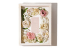 Decorative shadow box with color preserved flowers and a pink wedding invitation inside.