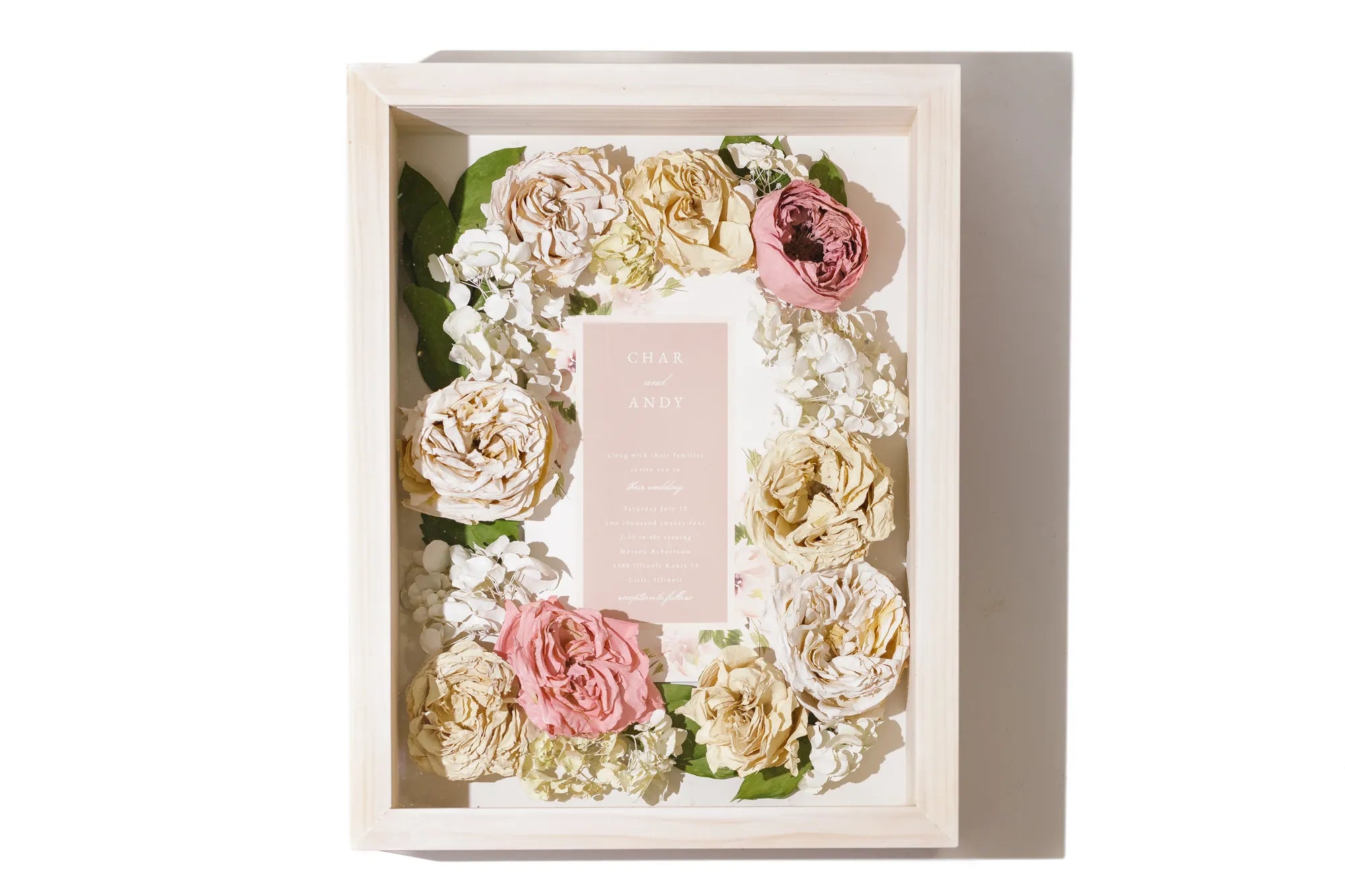 Decorative shadow box with color preserved flowers and a pink wedding invitation inside.
