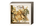 Preserved floral arrangement and keepsakes in a decorative shadow box with a white background