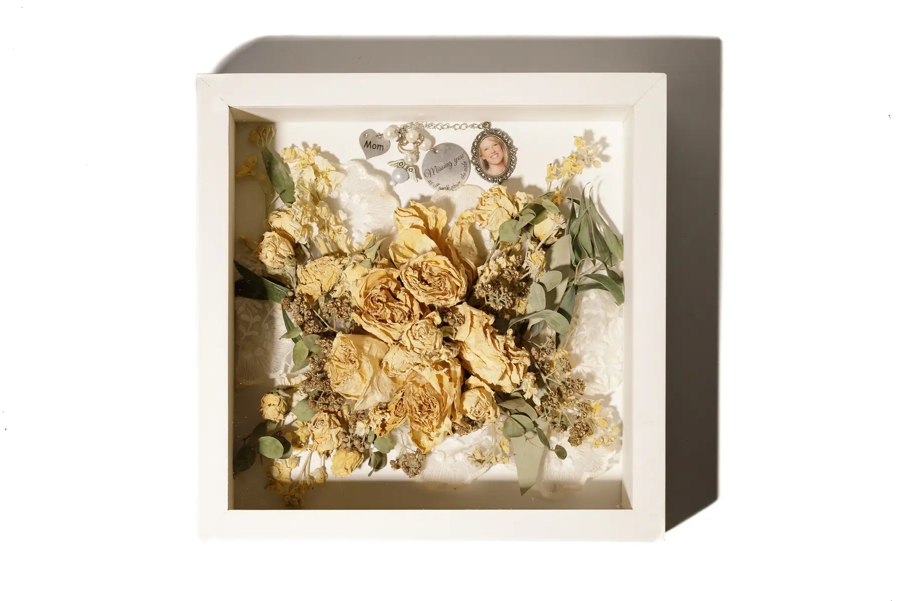 Preserved floral arrangement and keepsakes in a decorative shadow box with a white background