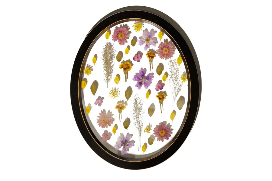 An oval handmade wooden black frame with a spaced design of pressed and preserved flowers with clear background