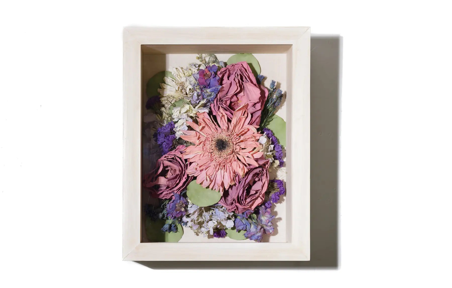 Preserved floral arrangement framed in a white wooden shadow box on a white background