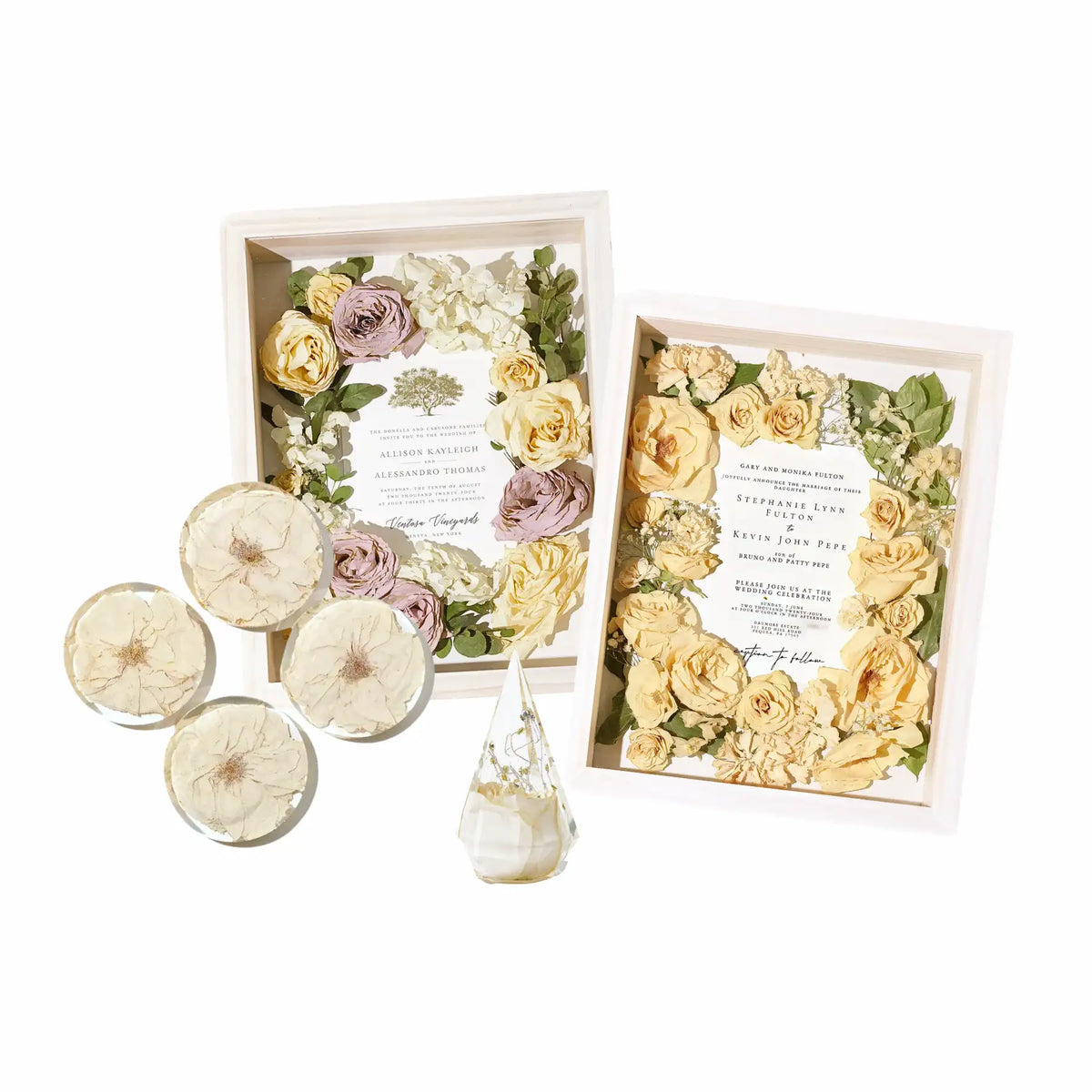 Two shadow box frames with preserved flowers surrounding wedding invitations and roses, four resin flower coasters, and a ring holder featuring a white flower.