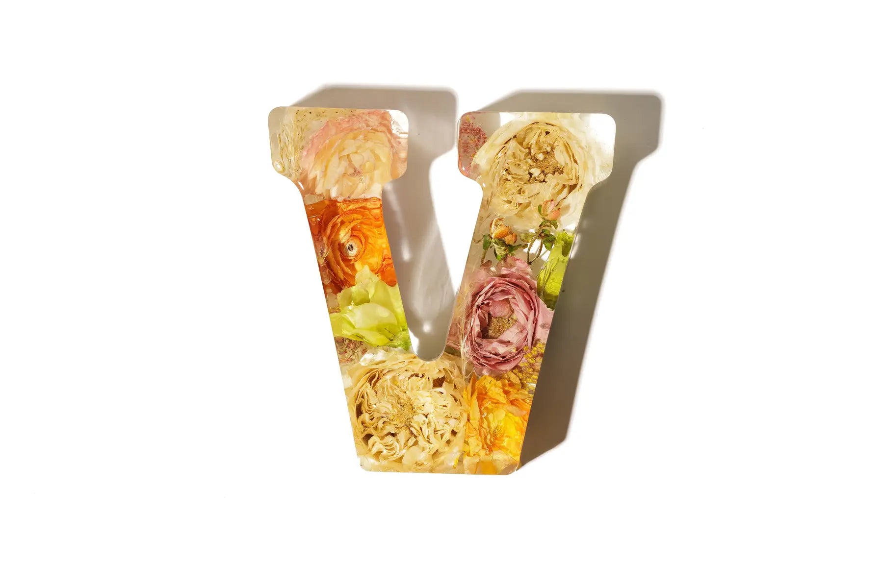 Small resin preservation letter 'V' made of light colored flowers on a white background