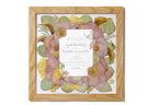 Framed wedding invitation surrounded by preserved pressed wedding flowers in a natural brown handmade frame