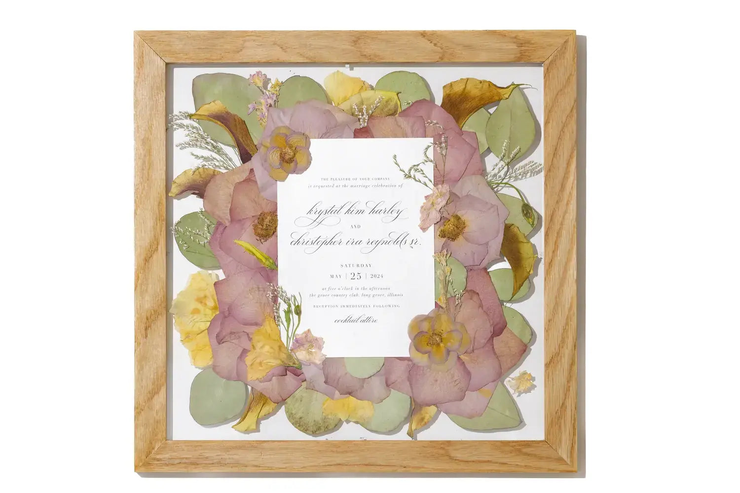 Framed wedding invitation surrounded by preserved pressed wedding flowers in a natural brown handmade frame