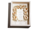 White handmade wooden shadow box featuring pink roses and a wedding invitation.